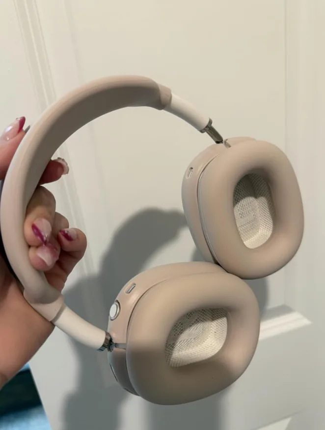 Hand holding sand-colored Apple AirPods Max headphones