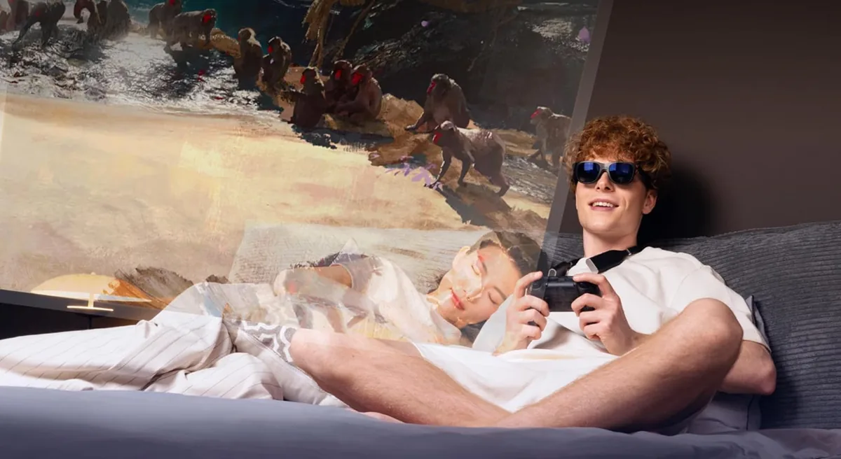Person relaxing in bed wearing AR display glasses with a game controller