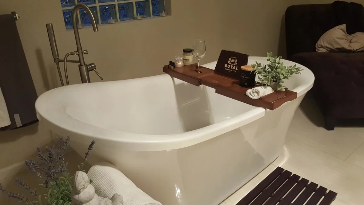 Bamboo bathtub caddy holding a wine glass, candle and plant across a freestanding tub