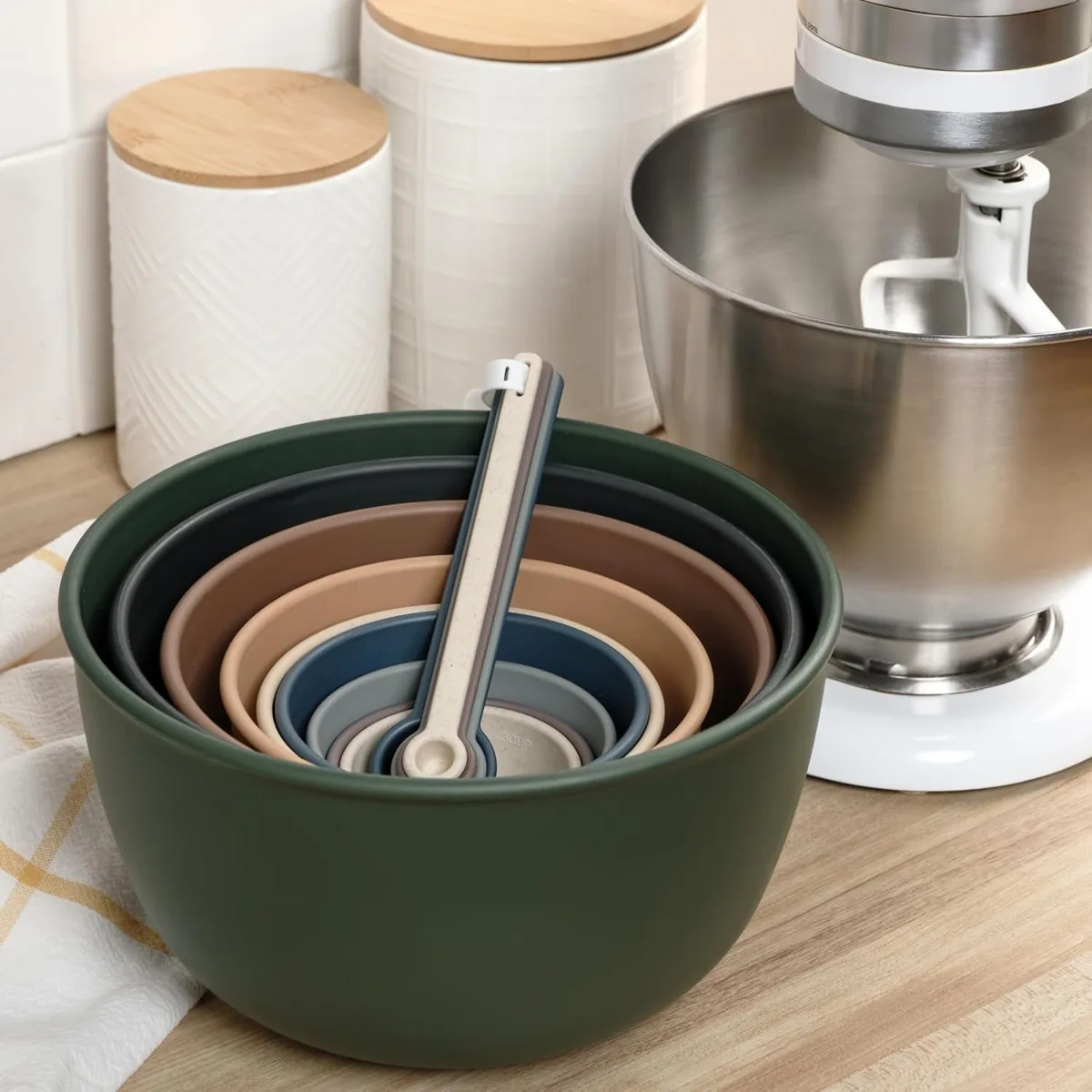 Nested colorful mixing bowls with measuring spoons beside a stand mixer on a kitchen counter