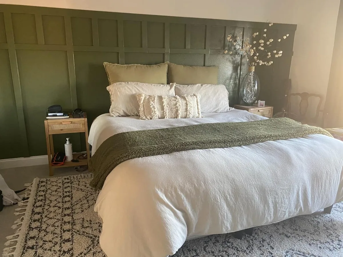 White linen duvet cover on a made bed against a green paneled wall