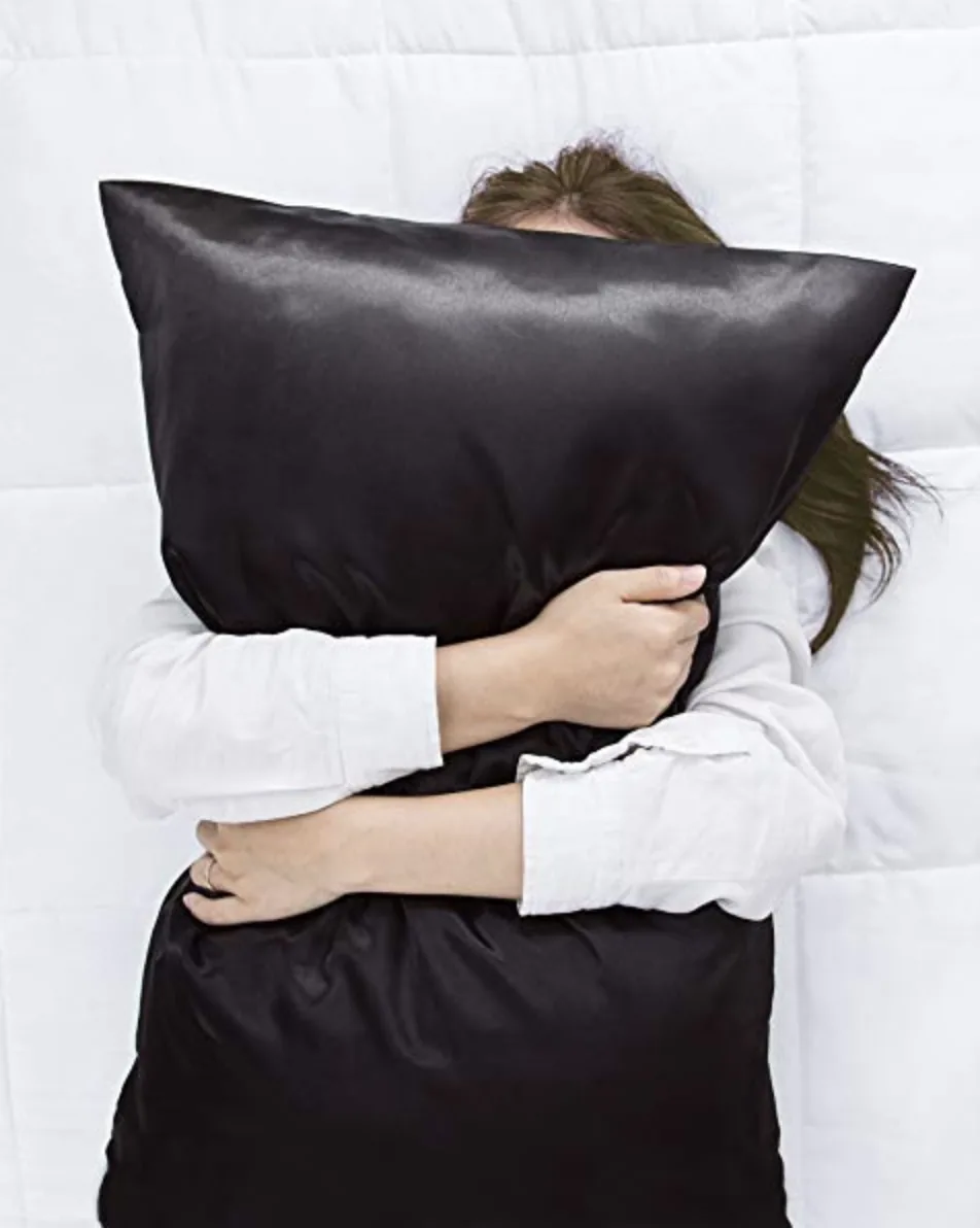 Person hugging a pillow in a black satin pillowcase