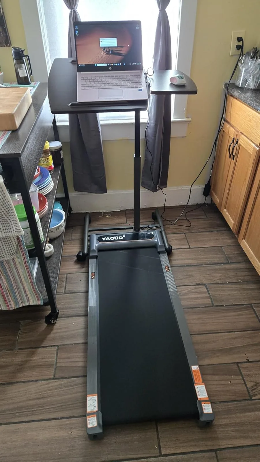 Black walking pad under a laptop stand in a home kitchen work setup