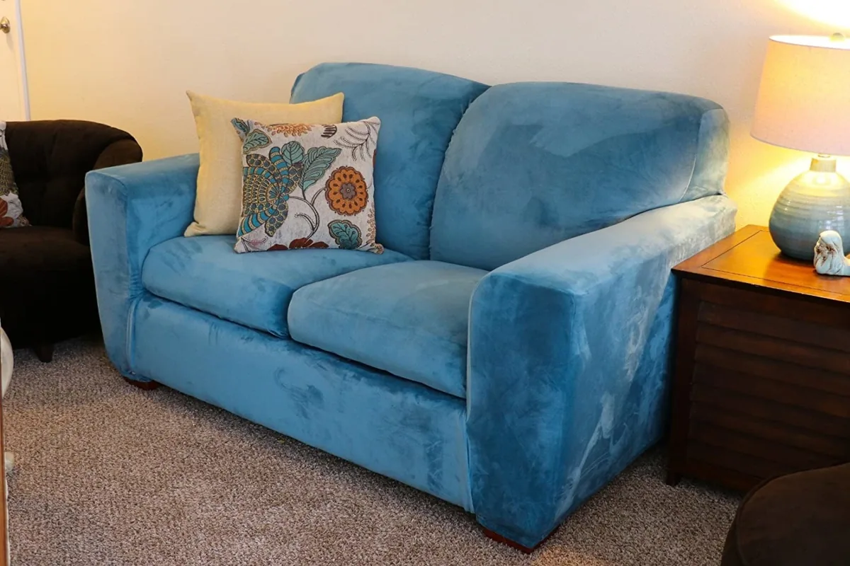 Loveseat dressed in a fitted blue velvet stretch slipcover with patterned pillows