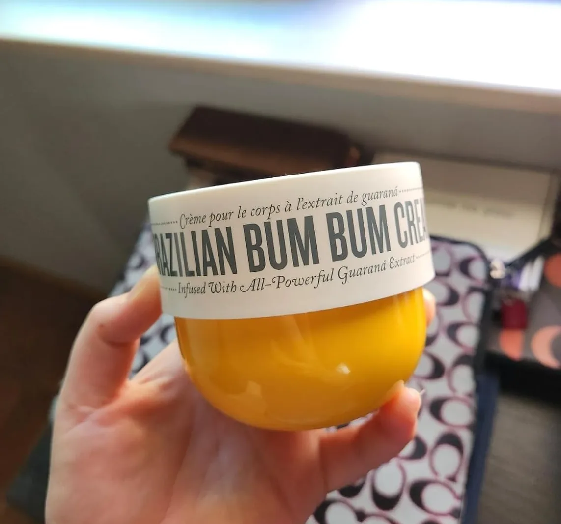 Hand holding an open jar of Brazilian Bum Bum body cream