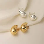Chunky teardrop earrings in polished gold and silver on cream fabric