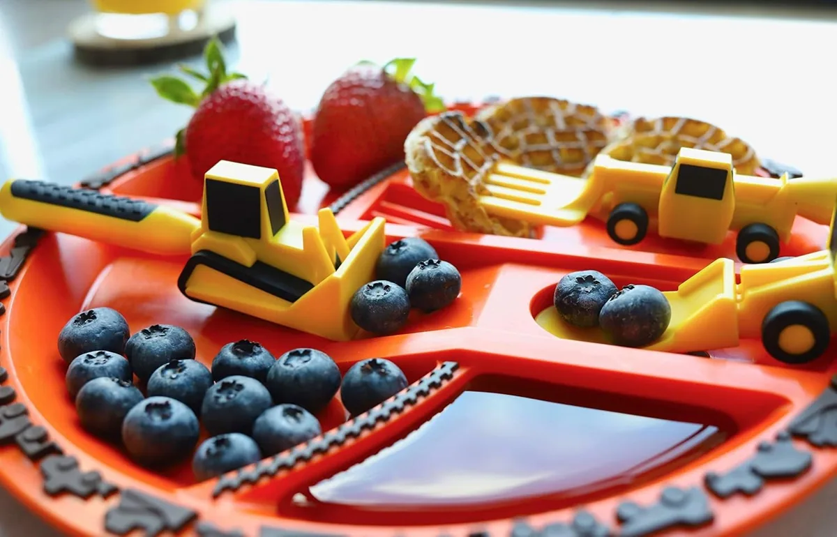 Orange divided toddler plate with bulldozer and loader utensils, berries and waffle pieces