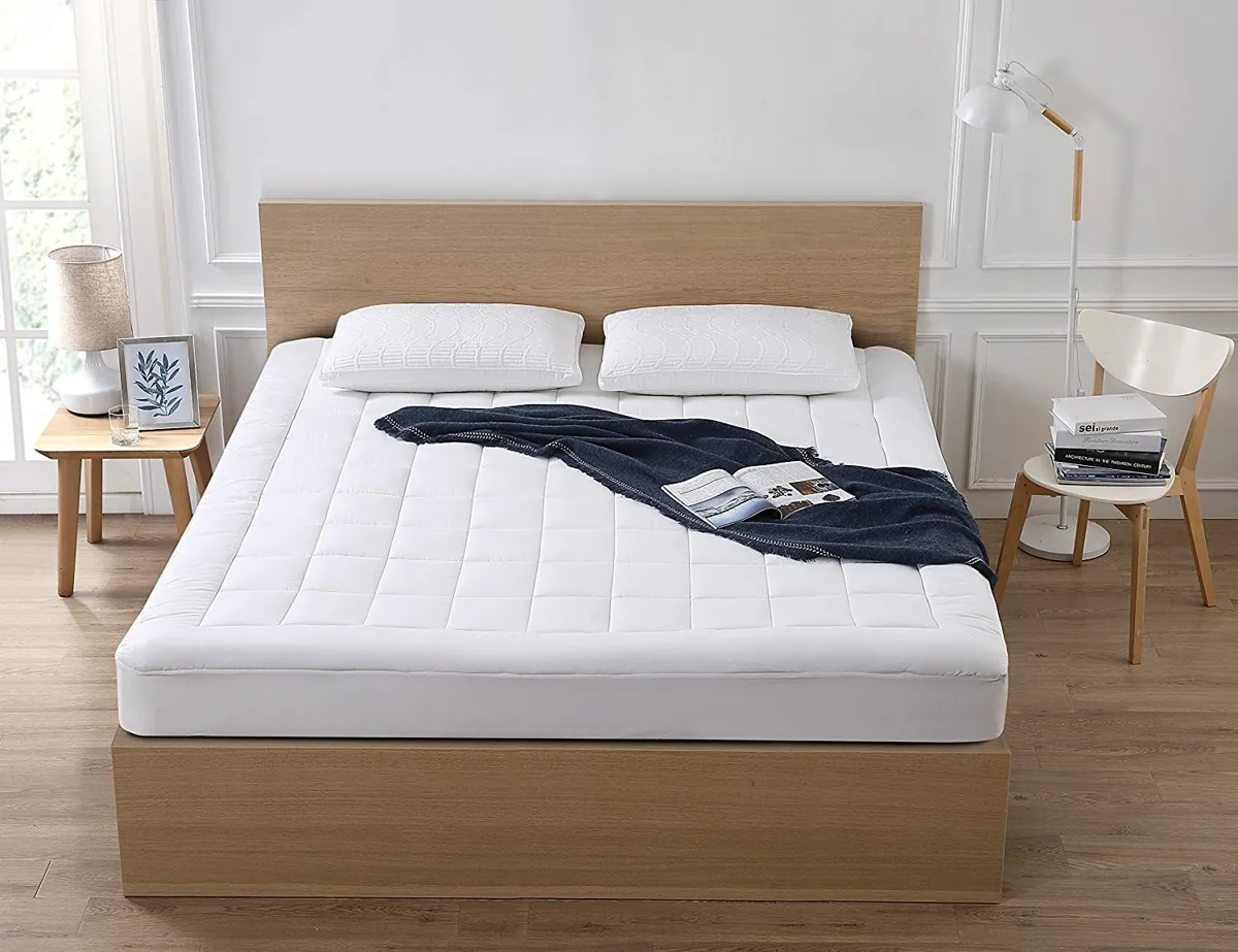 Quilted white cooling mattress topper on a wooden bed frame