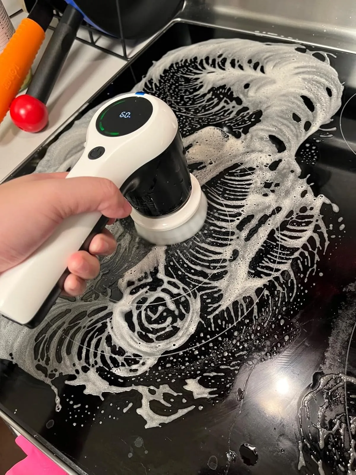 Hand using a cordless electric spin scrubber with soapy suds