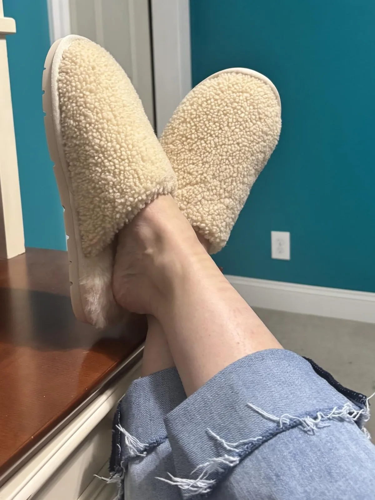 Feet crossed on a ledge wearing cream Cozy Earth shearling slippers