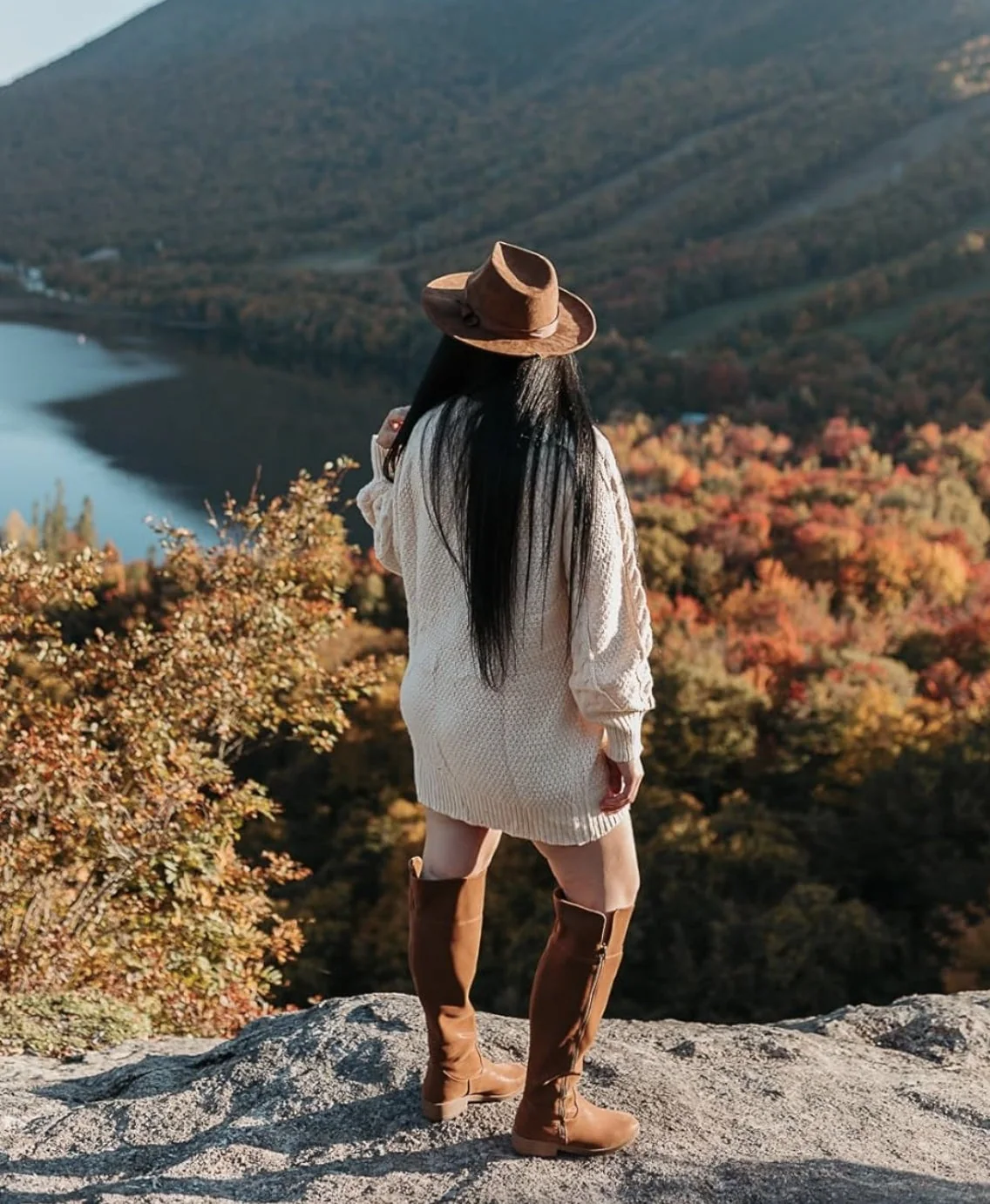 Cream sweater dress and tall boots against an autumn lake view