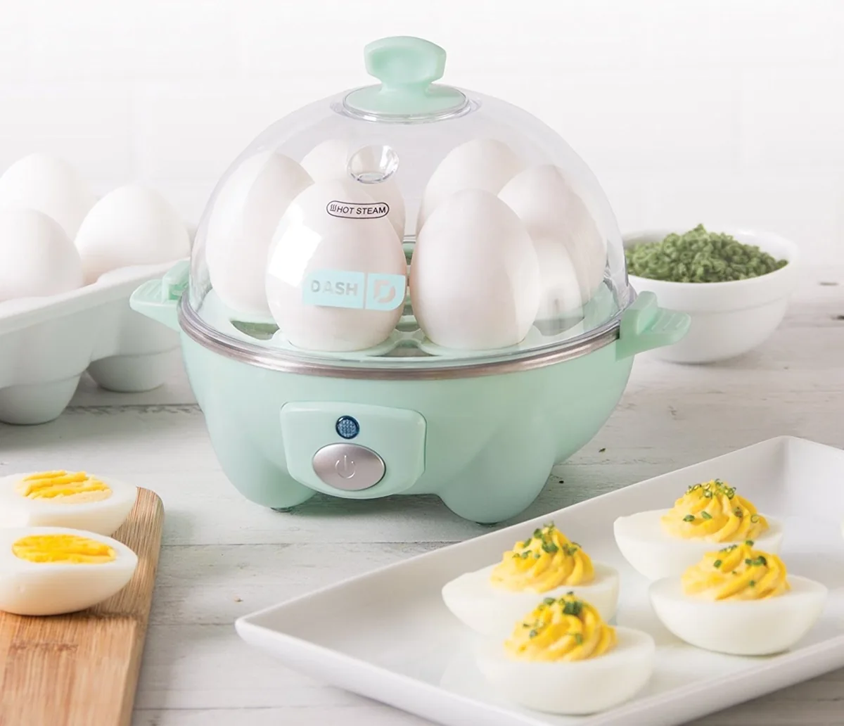 Aqua Dash rapid egg cooker filled with eggs next to a plate of deviled eggs