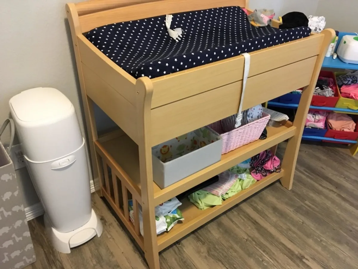 White Diaper Genie pail standing next to a wooden changing table in a nursery