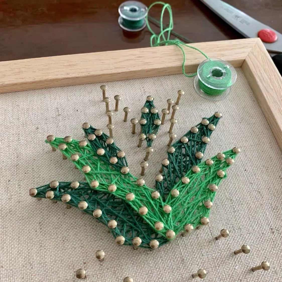 String art project in progress with green thread wrapped around nails in a wooden frame
