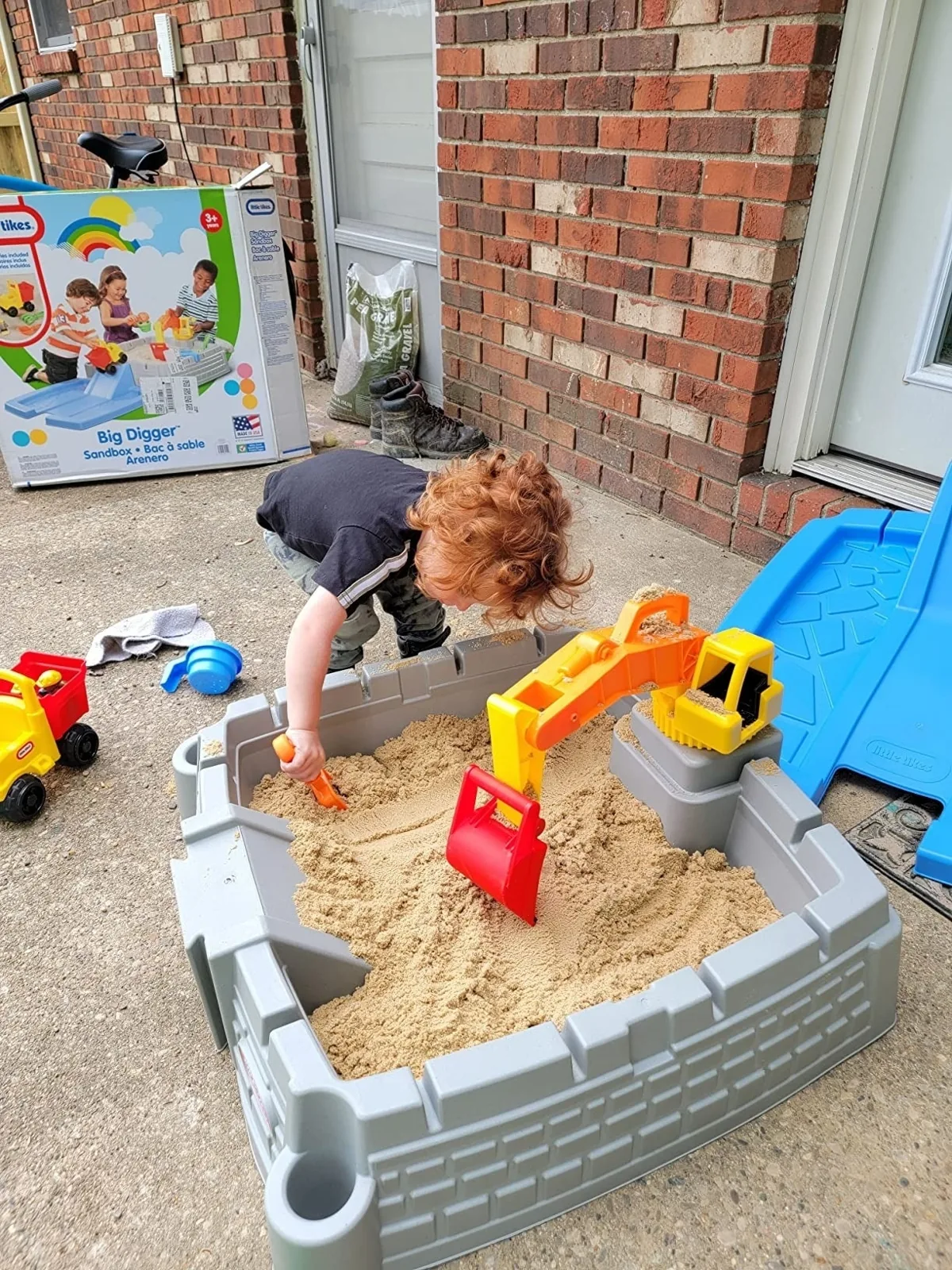 Child digging in a sandbox with a built-in toy excavator