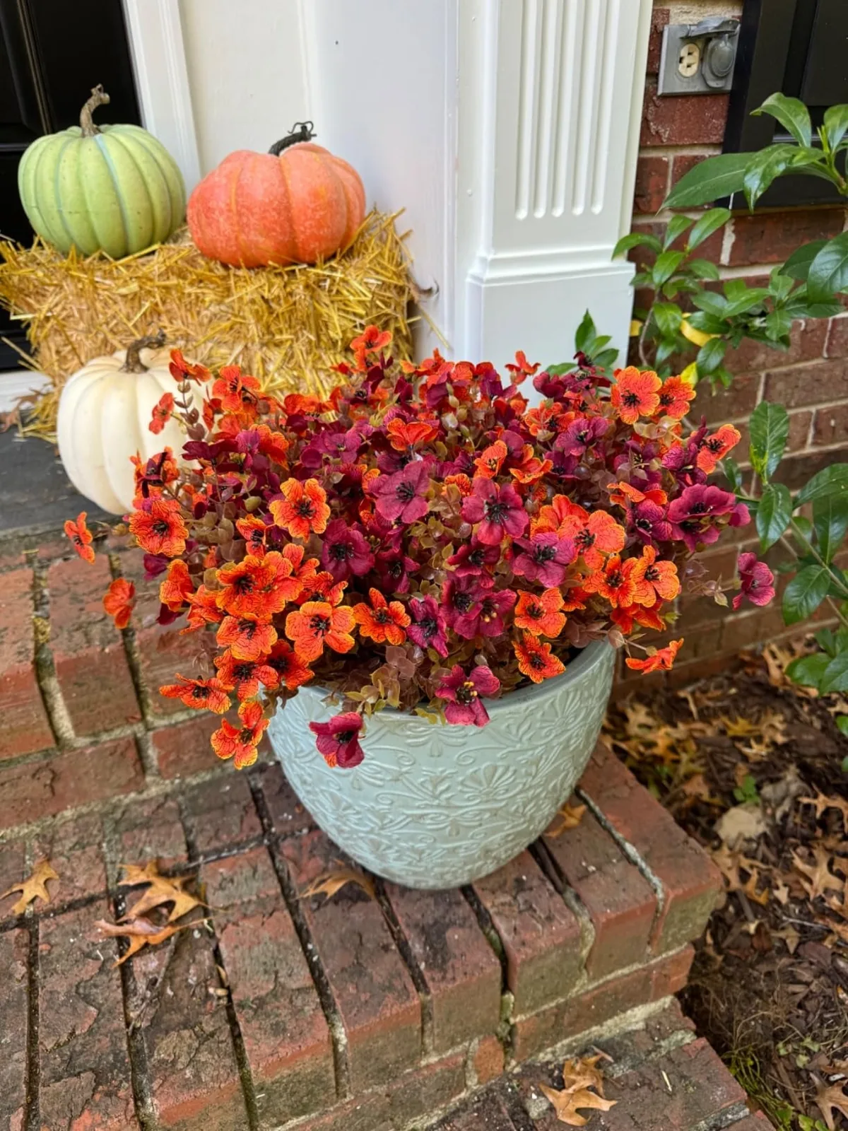 Faux orange and brown mums potted beside pumpkins on hay