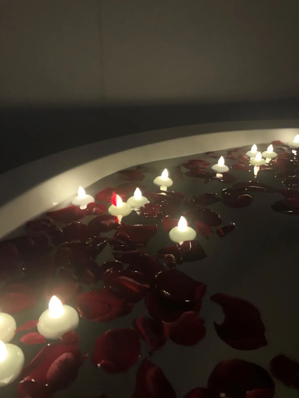 Floating LED tealights glowing among rose petals in a dark bath