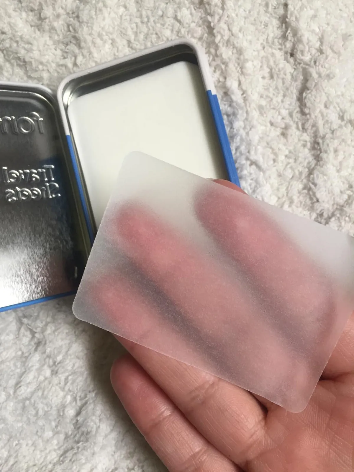 Hand holding a paper soap sheet above a tin full of soap sheets