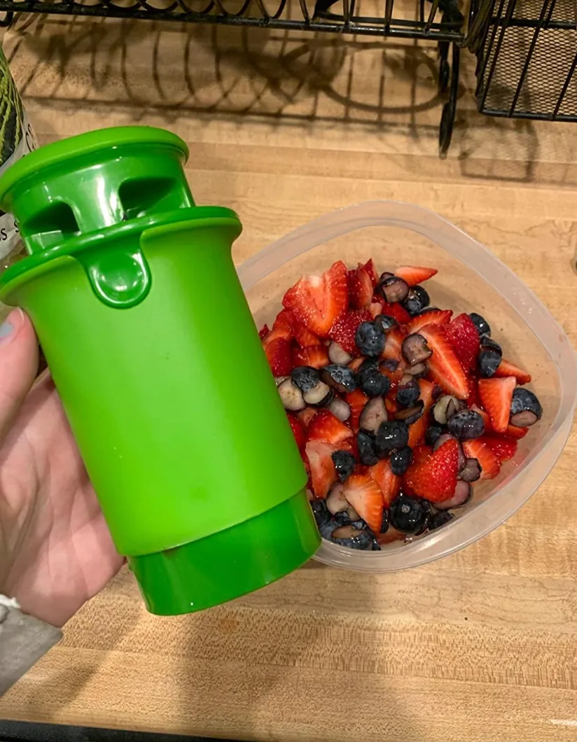 Green fruit and veggie divider held next to a container of halved fruit