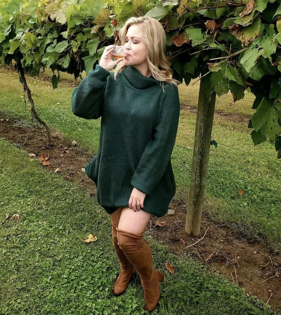 Forest green oversized turtleneck sweater dress worn with tan over-the-knee boots in a vineyard