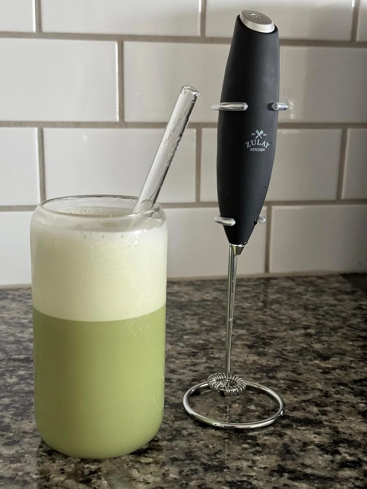 Black handheld electric milk frother next to a glass of frothy matcha latte