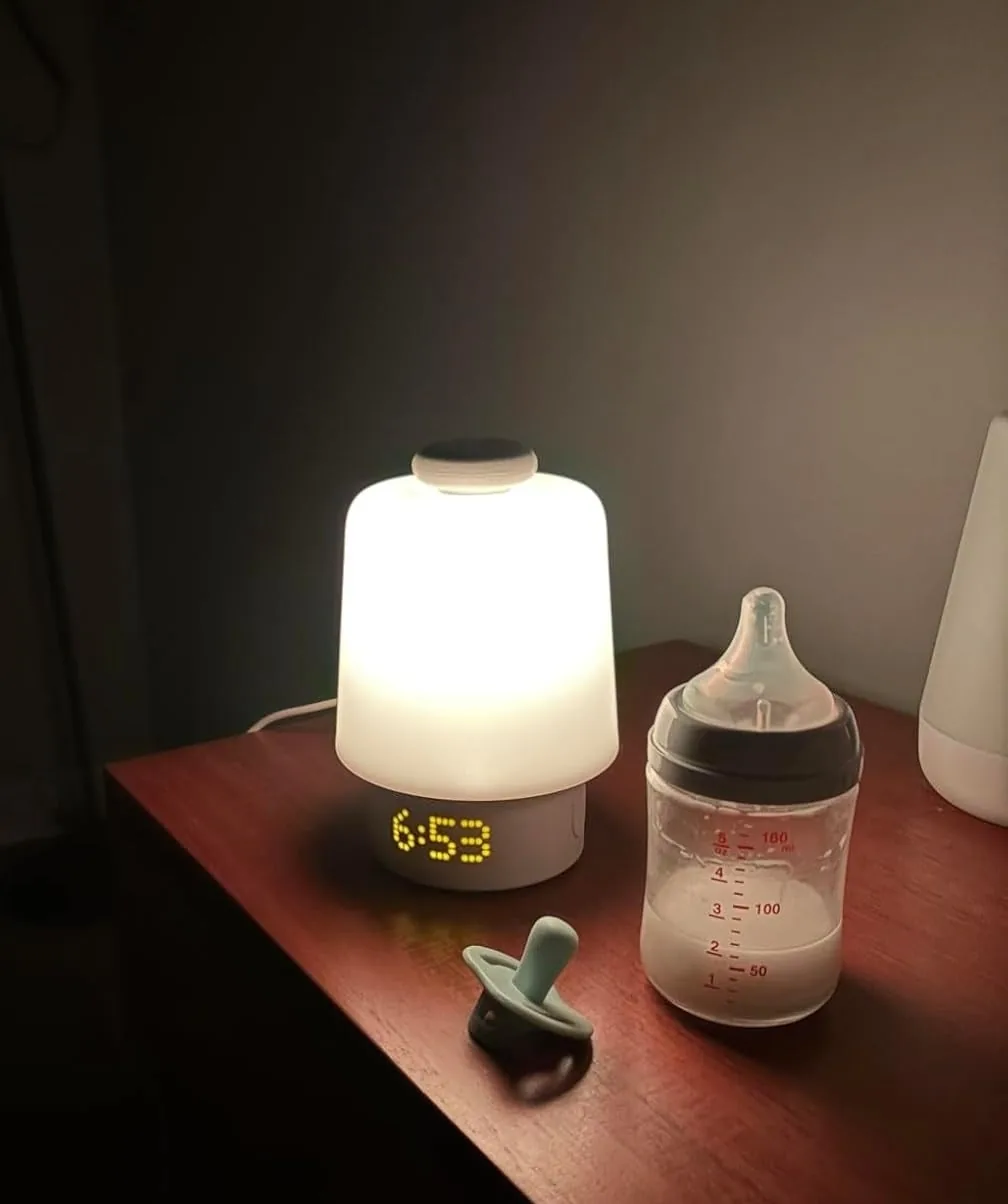 Hatch sound machine glowing as a night-light with its clock on, beside a bottle and pacifier