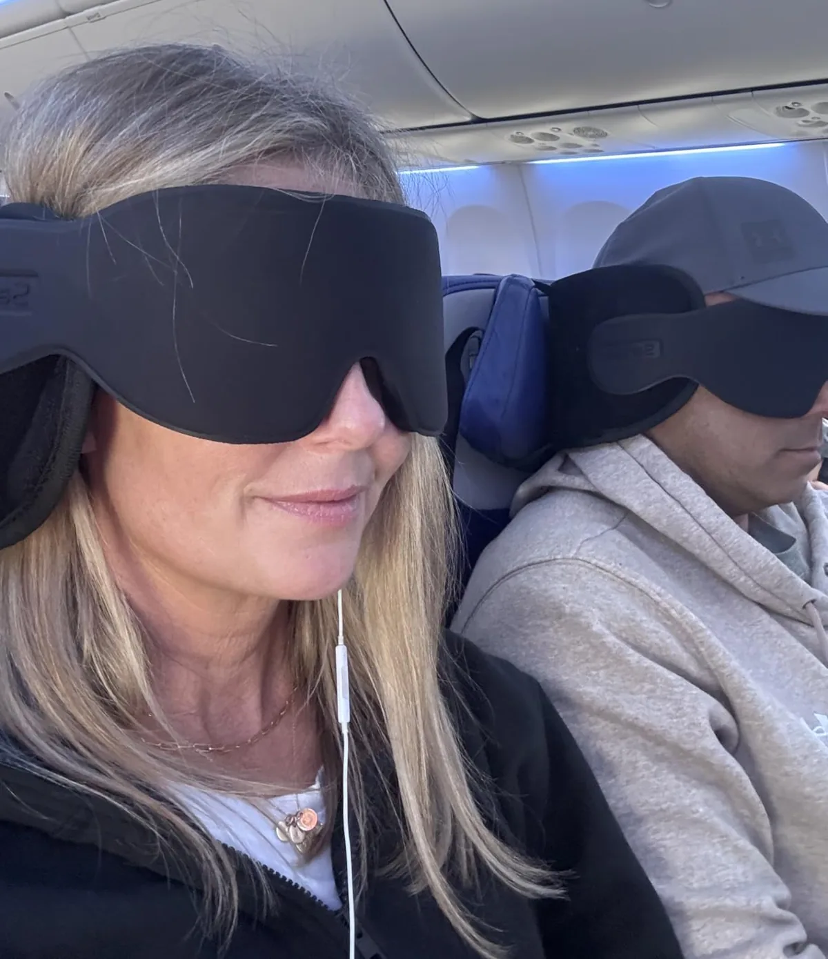 Travelers on a plane wearing a headrest neck pillow with a padded eye mask