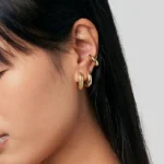 Close-up of a woman wearing textured gold hoop earrings and a gold ear cuff