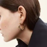Woman wearing a wavy twisted gold hoop earring with a dark blazer