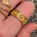 Hand wearing a wide gold ring engraved with a moon, star and sun, stacked with other gold rings