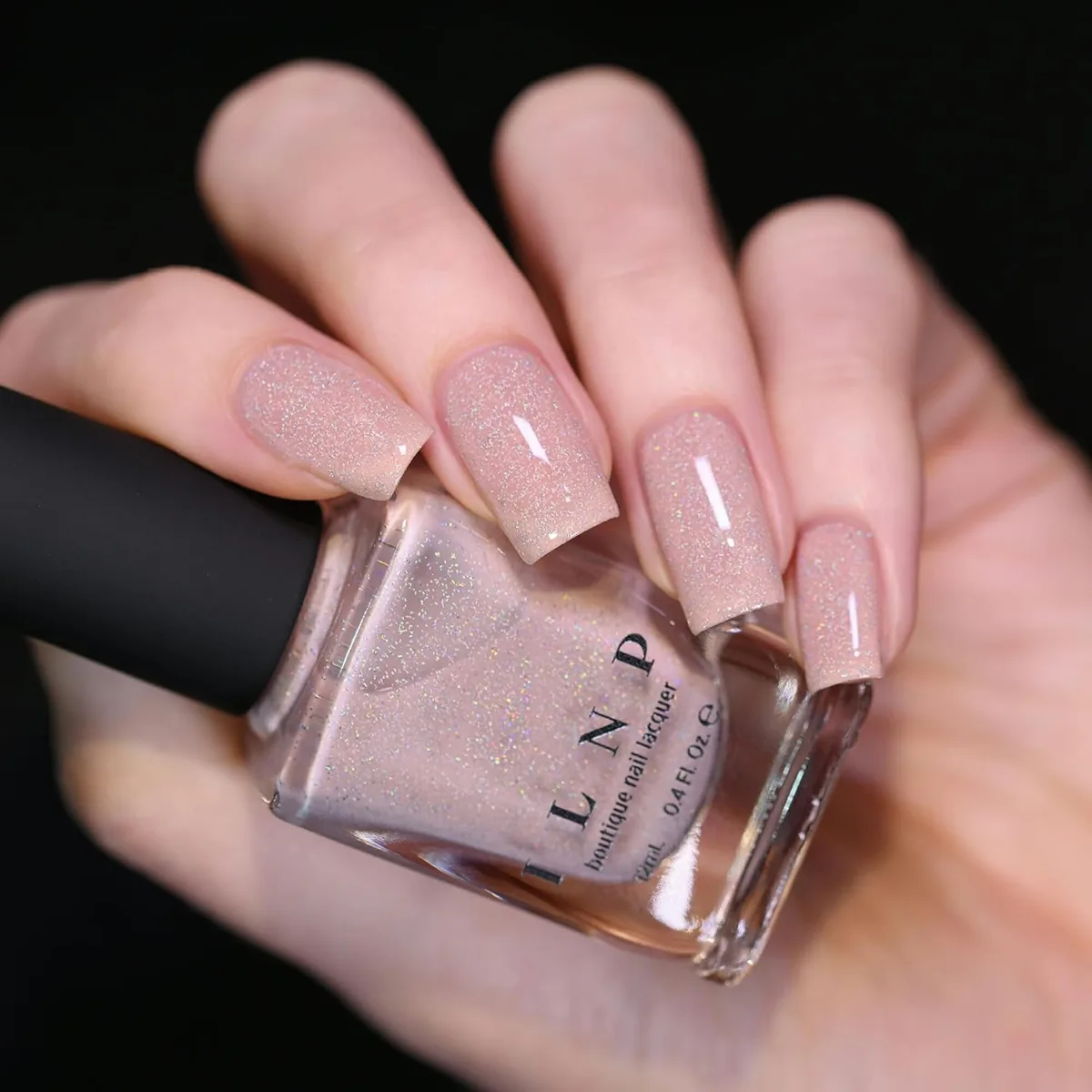 Hand holding a bottle of ILNP Birthday Suit, a sheer nude polish with shimmer