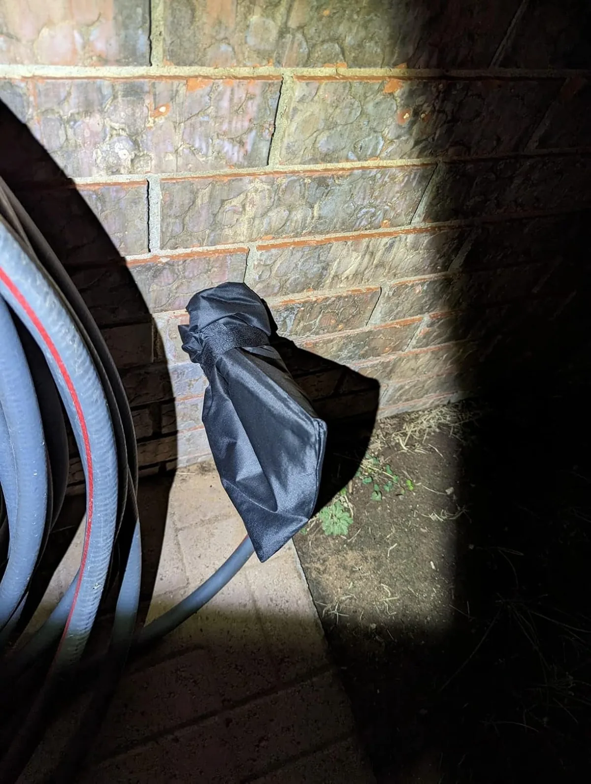 Black insulated cover over an outdoor faucet on a brick wall