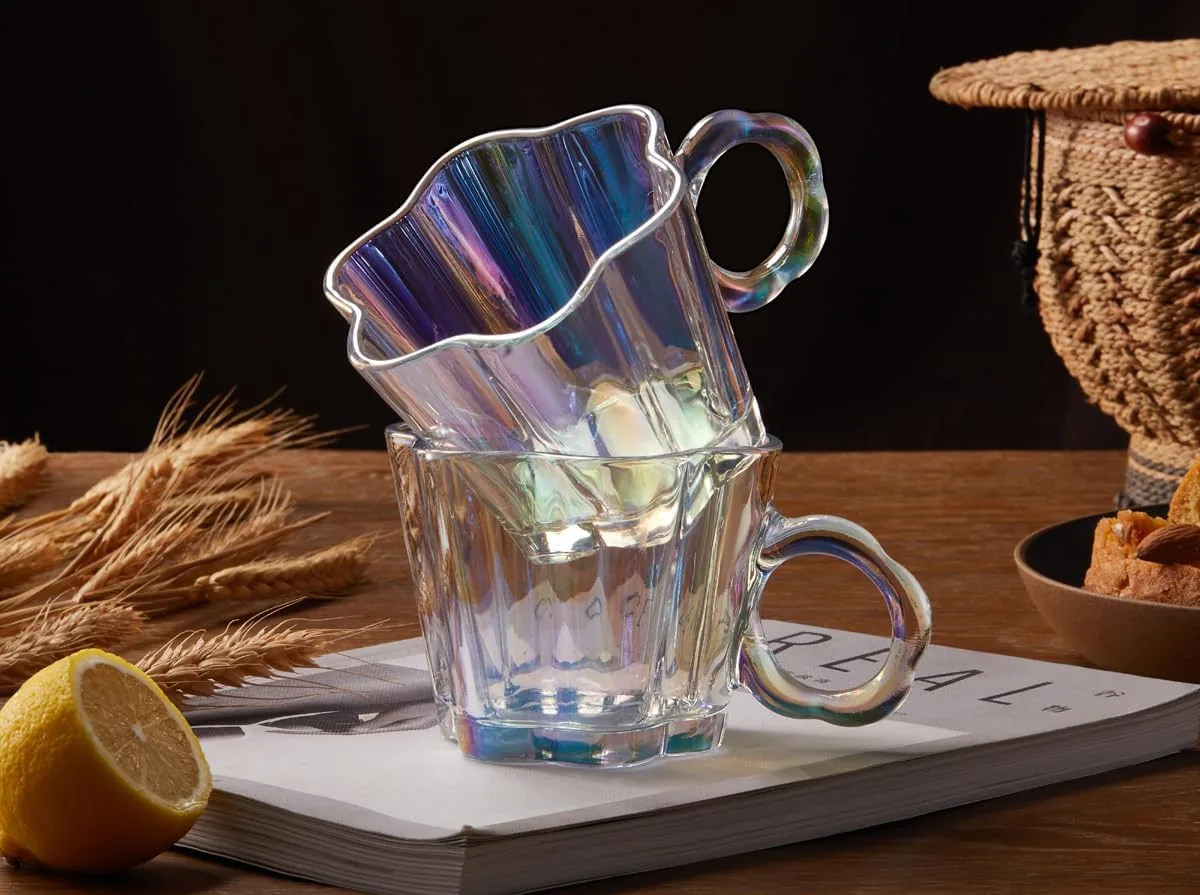 Two iridescent scalloped glass coffee mugs stacked on a book on a wooden table