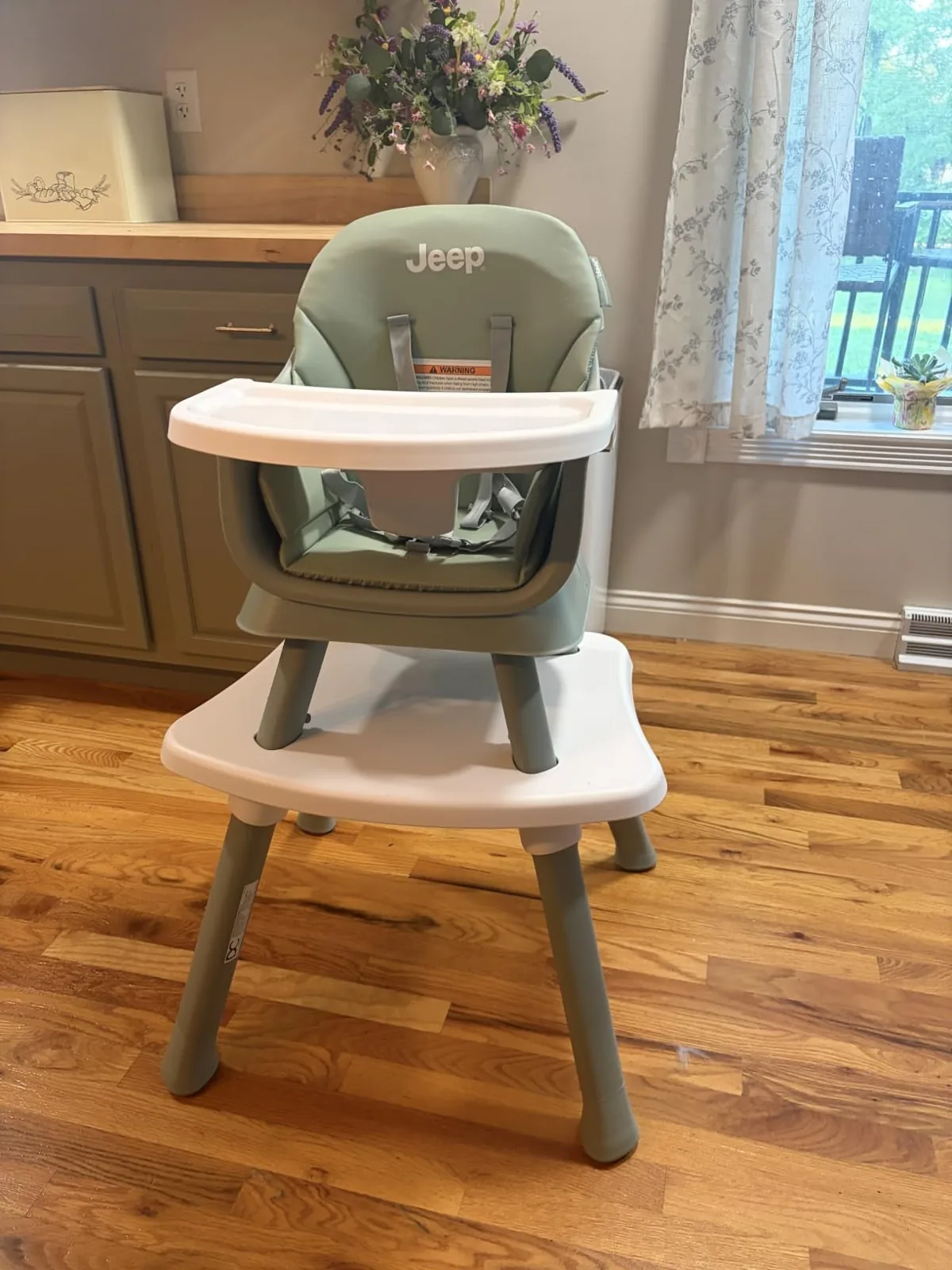 Sage green Jeep Milestone convertible high chair with detachable tray on a wood floor