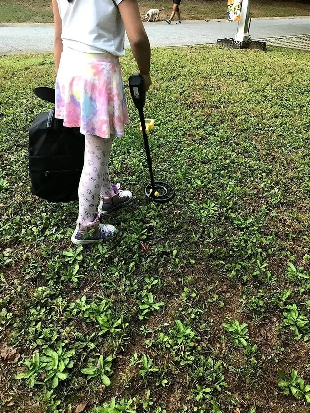 Child sweeping a yellow kids metal detector over grass