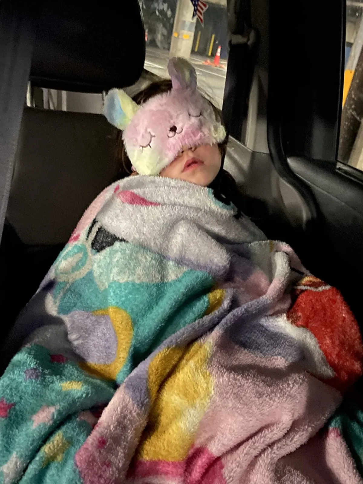 Child napping in a car seat wearing a soft unicorn sleep mask