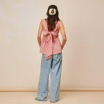 Woman wearing a gingham babydoll top with a large back bow, loose jeans and a floral hair accessory