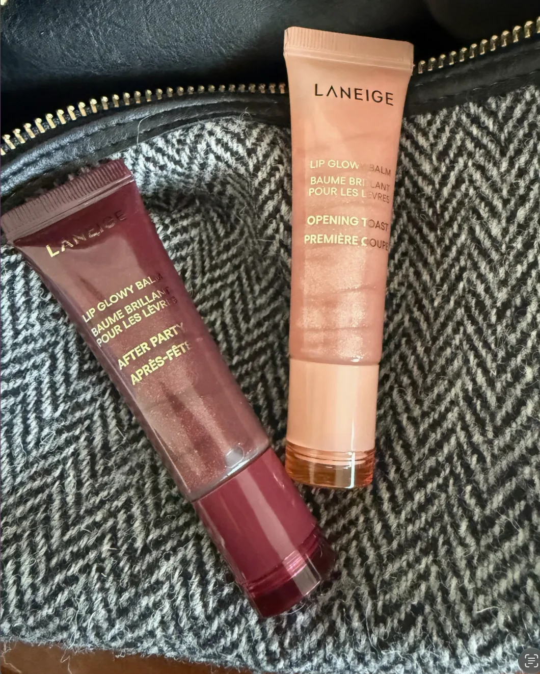 Two LANEIGE Lip Glowy Balm tubes in After Party and Opening Toast shades on a tweed bag