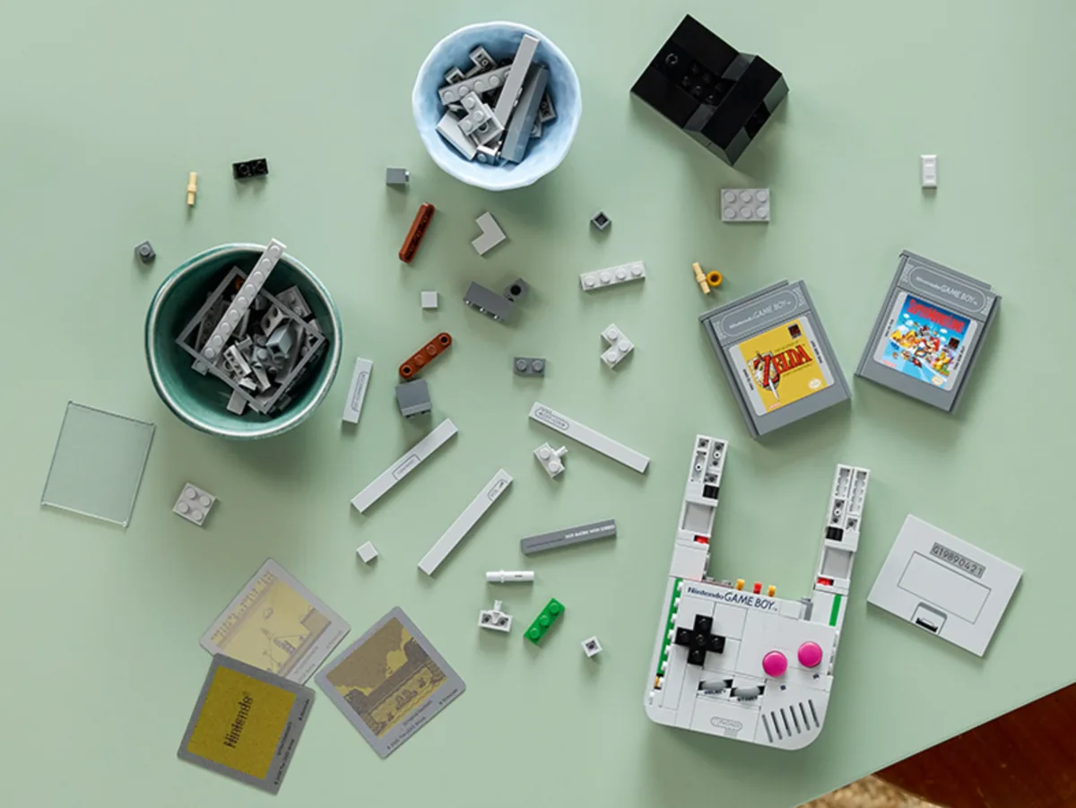 LEGO Game Boy partially built among loose bricks and game cartridge pieces on a green table