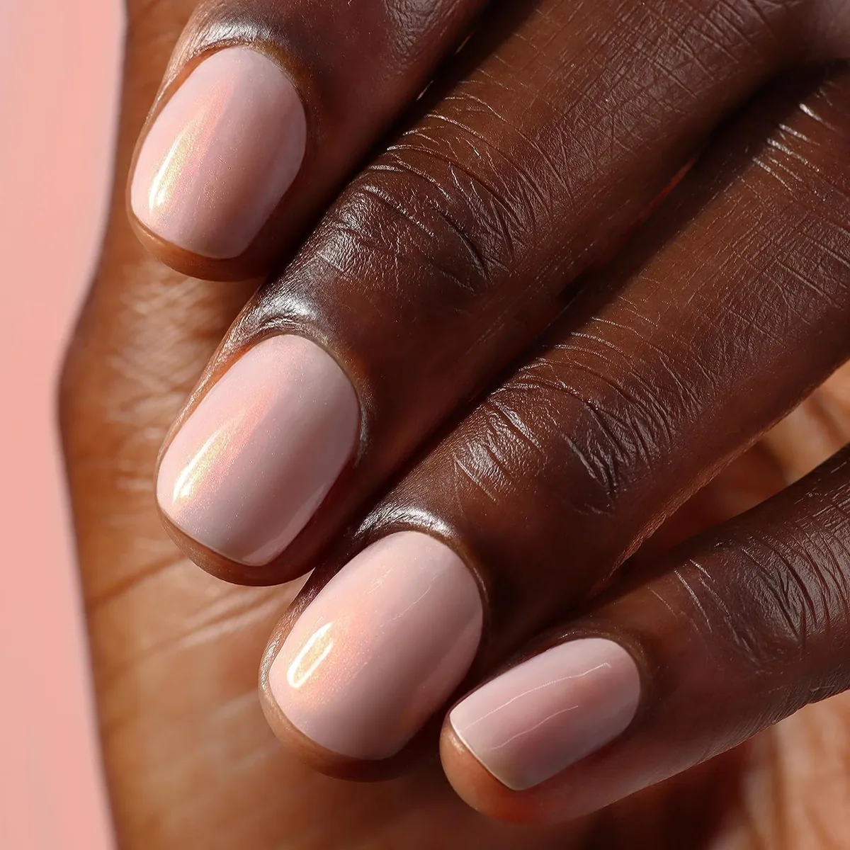 Close-up of short nails painted in a sheer, glowing pink nail concealer