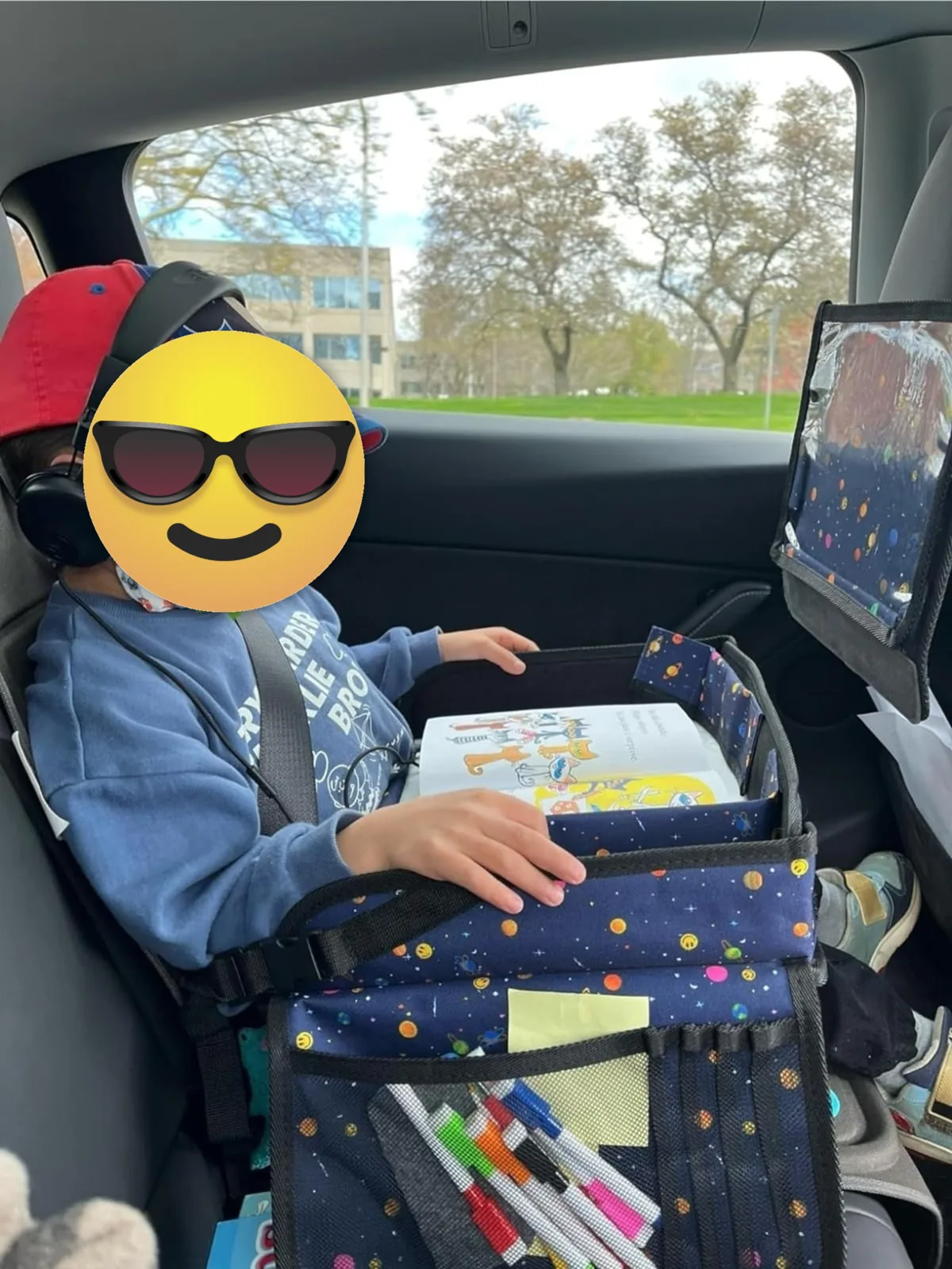 Child in a car seat using a travel activity tray with dry-erase surface