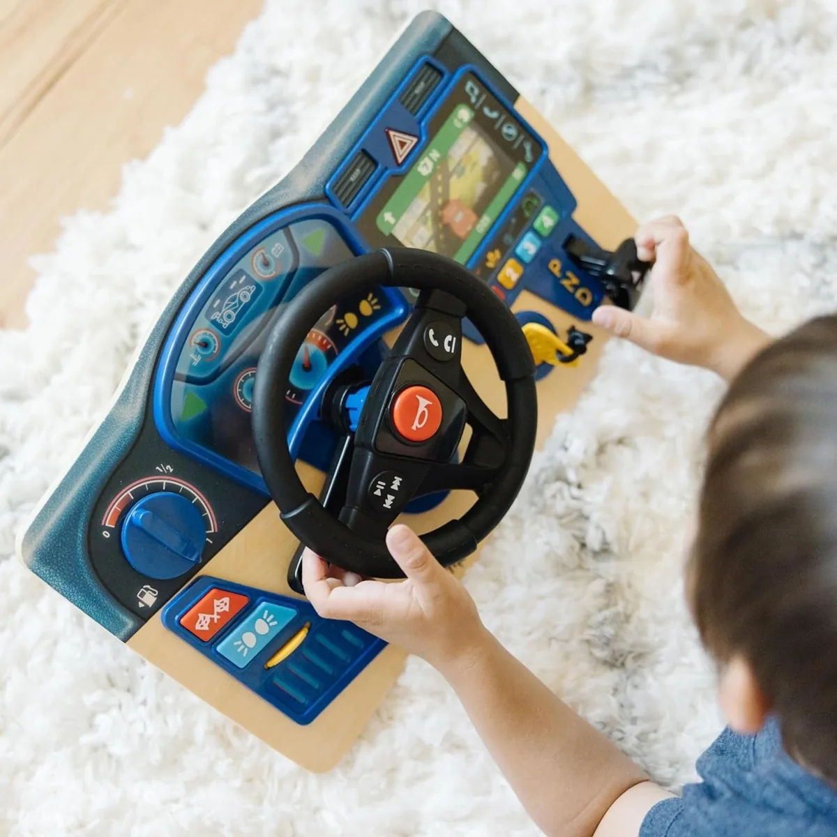 Child steering the wheel of a wooden toy car dashboard with buttons, a gear stick and screen