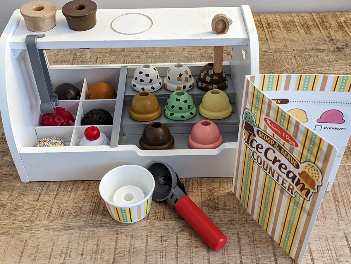 Wooden toy ice cream counter with colorful scoops, toppings, a cup and scooper