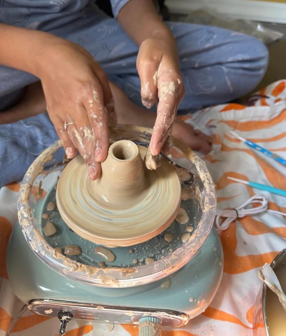 Hands shaping clay on a mini pottery wheel
