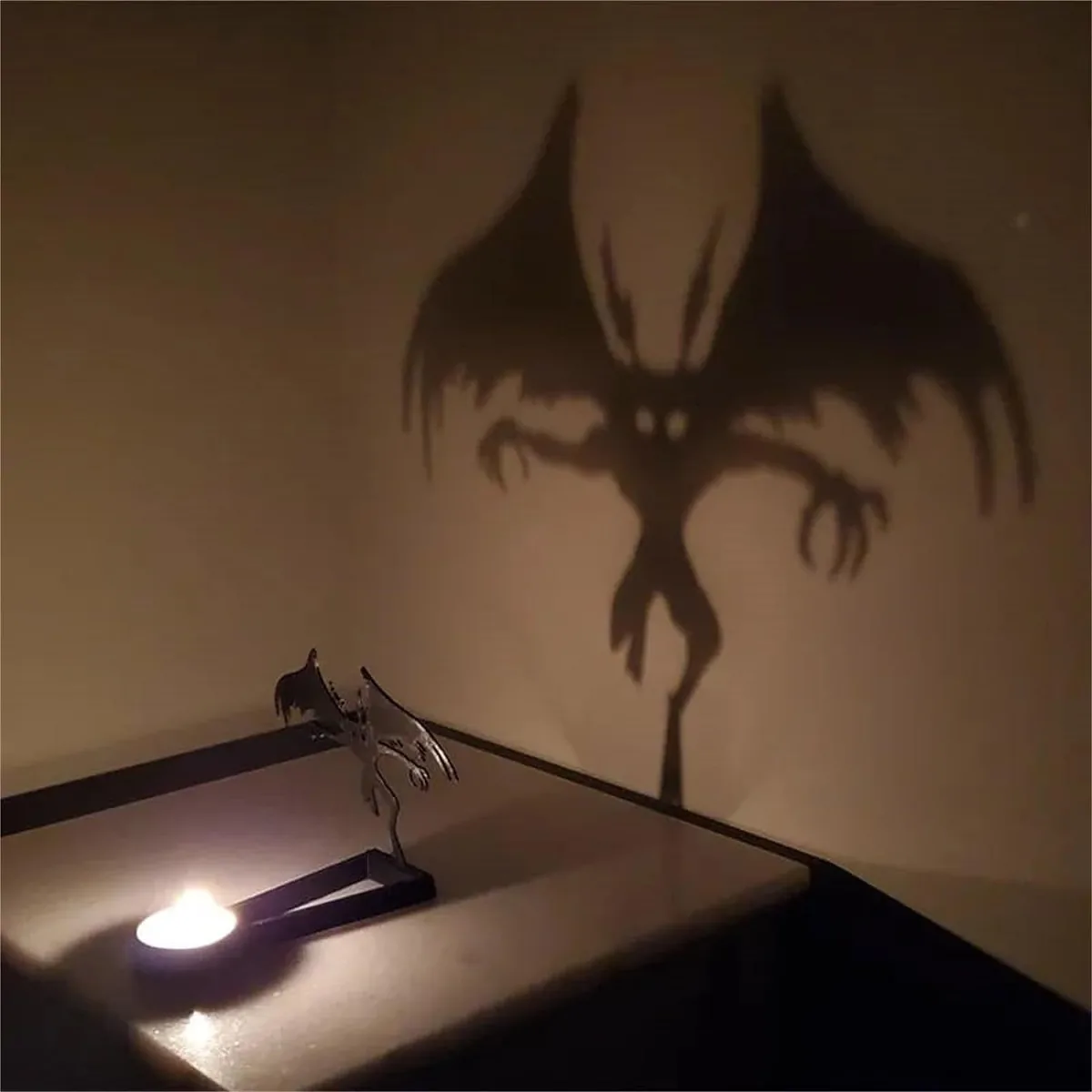 Metal tea light holder casting a large winged monster shadow on a wall