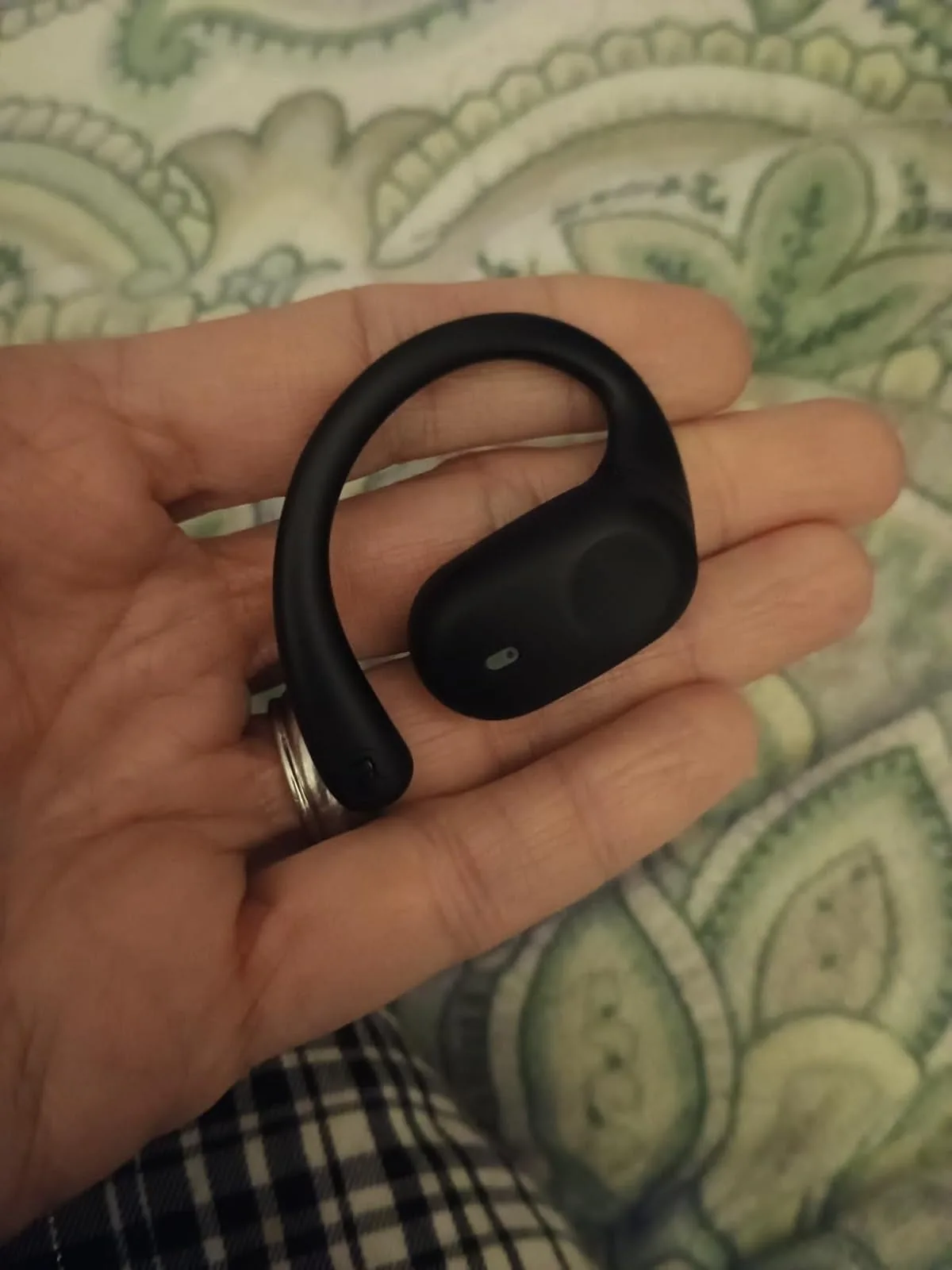 Black open-ear sport earbud with an ear hook resting in a palm
