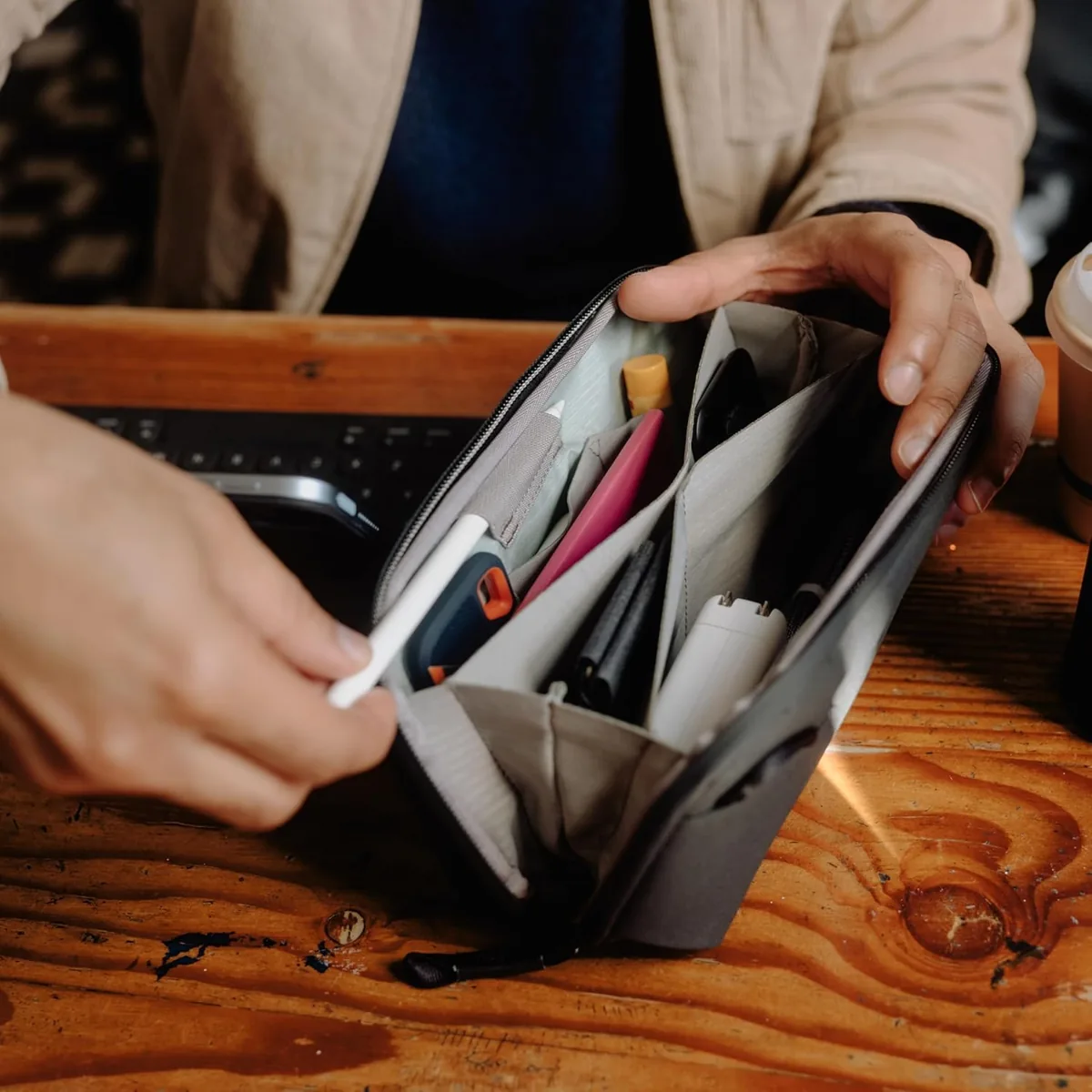 Hands opening a grey Peak Design tech pouch with folded pockets holding cables and chargers
