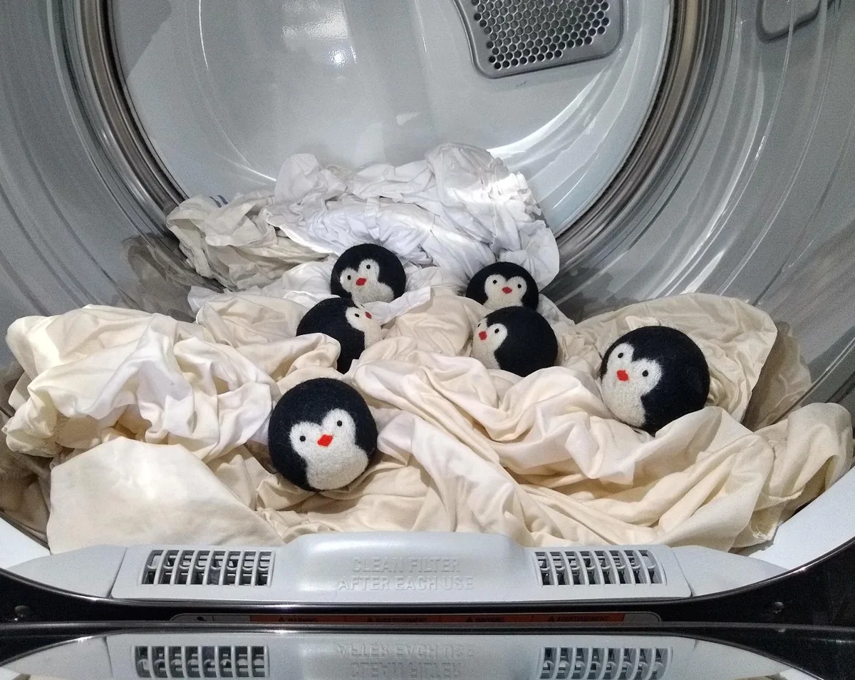 Penguin-shaped wool dryer balls resting on clean laundry inside a dryer drum