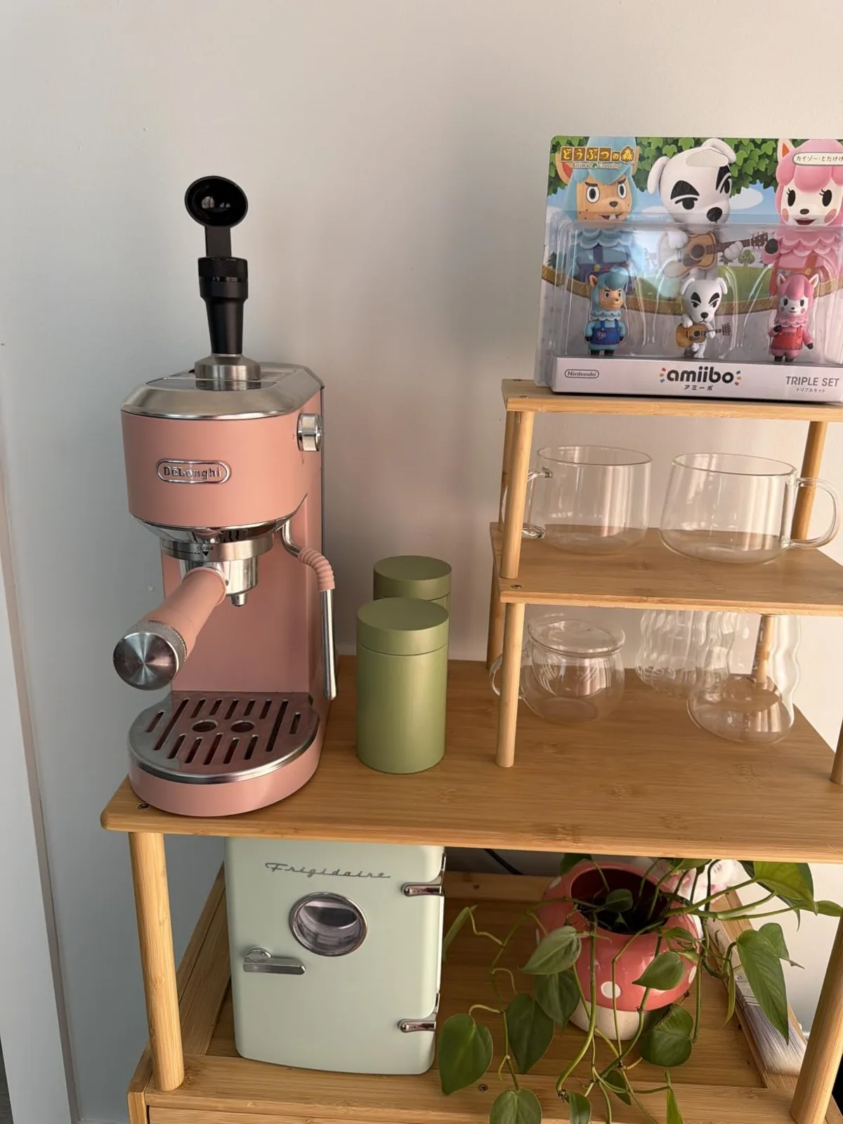 Pink compact espresso machine on a wooden coffee shelf with glass mugs