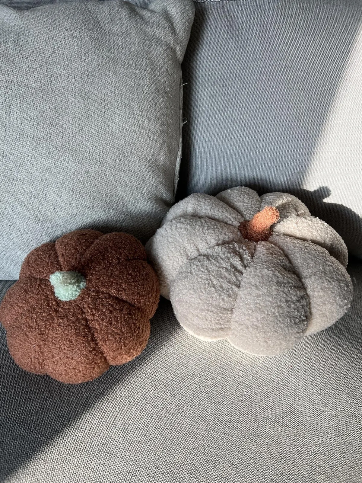 Two fuzzy off-white pumpkin shaped pillows on a sofa